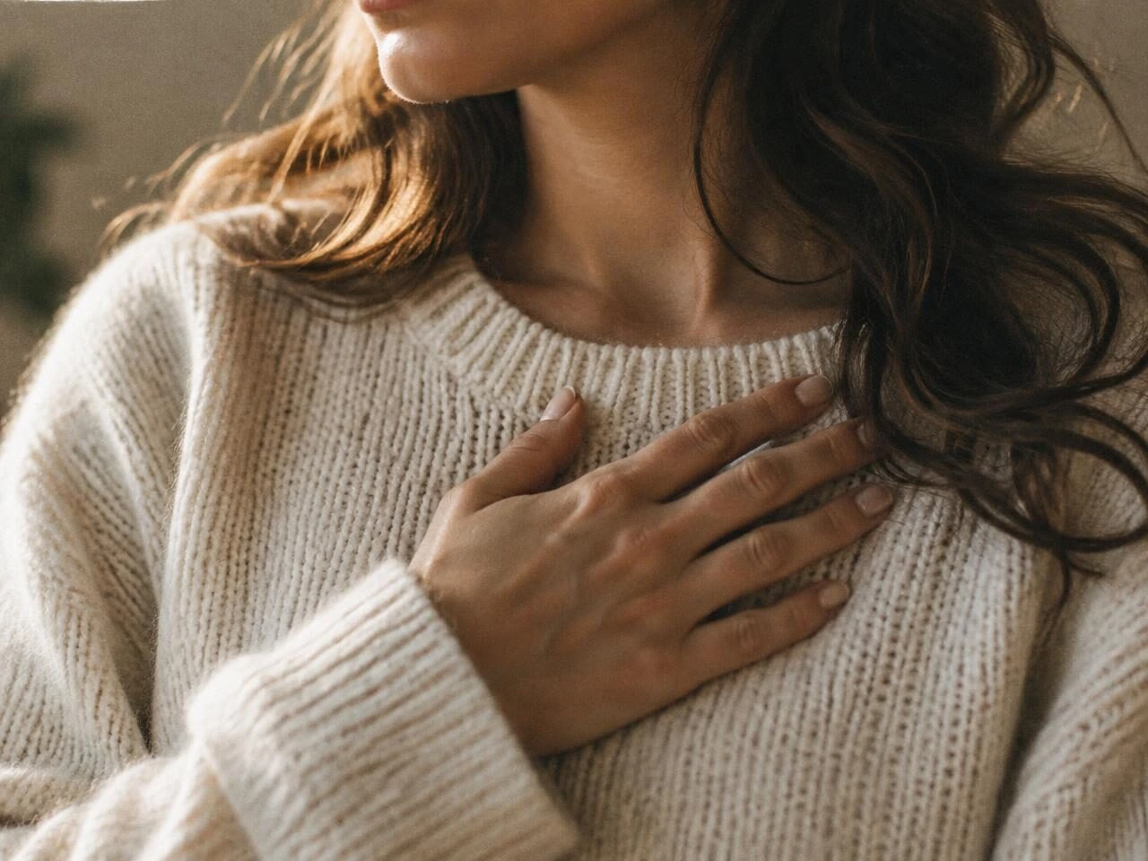 A woman's hand resting over her heart in soft light